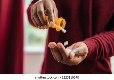 african american man in red shirt pouring pills from prescription pill bottle