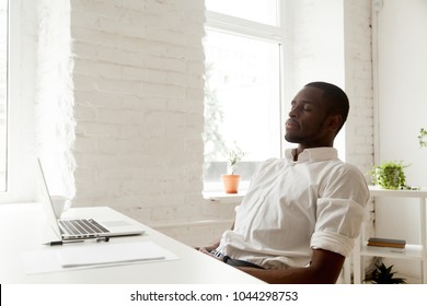 African American Man Relaxing After Work Breathing Fresh Air Sitting At Home Office Desk With Laptop, Black Relaxed Entrepreneur Meditating With Eyes Closed For Increasing Productivity At Workplace