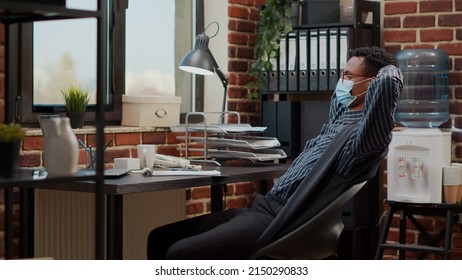 African american man relaxing on break after finishing commercial work. Employee talking pause from sales report planning in startup office, wearing face mask. Company job timeout