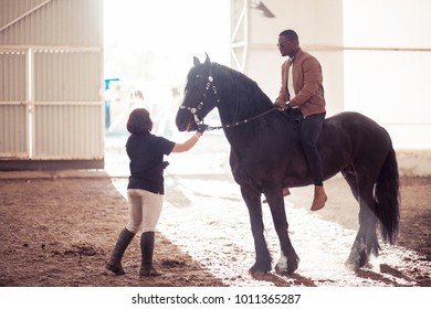 african american man riding black horse in hangar - Powered by Shutterstock