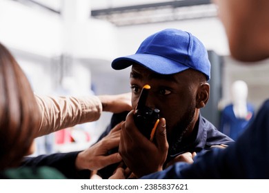 African American man security guy using walkie-talkie while holding back crowd of shoppers. Police officer managing large group of people at store entrance during busy holiday shopping seaso