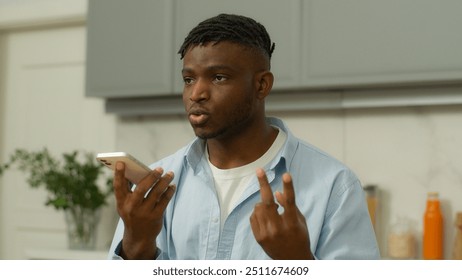 African American man serious biracial male hold smartphone using speaker phone speaking talk to cellphone loudspeaker comfort usage counting with fingers guy record voice message voicemail at kitchen - Powered by Shutterstock