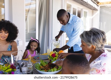 African american man serving drinks to multiracial family while having lunch at dining table at home. Multigeneration, meal, unaltered, togetherness, love, childhood, lifestyle and retirement. - Powered by Shutterstock