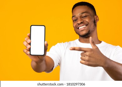 African American Man Showing Mobile Phone Screen Recommending App Smiling To Camera Posing Over Yellow Studio Background. Mockup