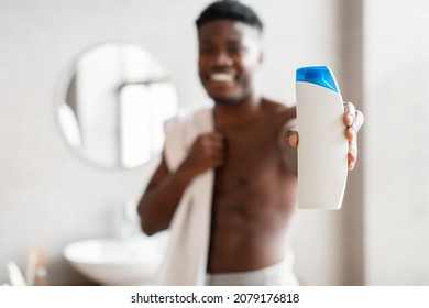 African American Man Showing Shampoo Bottle Standing Wrapped In Towel In Modern Bathroom At Home. Unrecognizable Guy Advertising Shower Gel. Male Beauty Products. Selective Focus