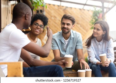 African American man showing thumb up, telling story to interested attentive friends, sitting, drinking coffee in cafe together, smiling multiethnic friends discussing, talking, chatting - Powered by Shutterstock