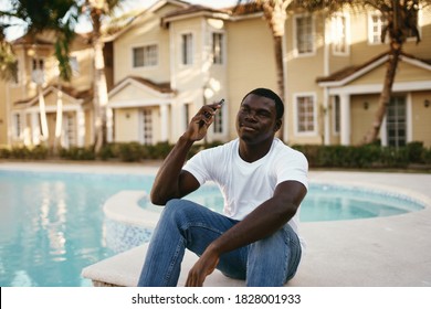 An African American Man Sits Near The Pool With A Mobile Phone In His Hand In Nature