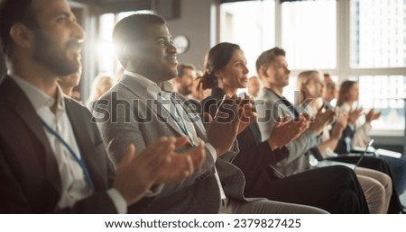 African American Man Sitting in Crowded Auditorium at a Tech Conference. Black Businessman Listening To Keynote. Specialist Watching Innovative Technology Presentation And Clapping With Audience.