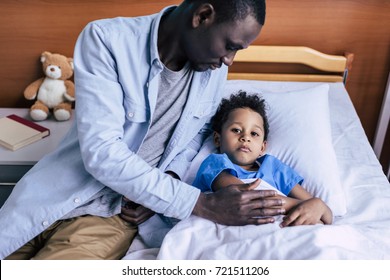 African American Man Sitting Near Sick Son Lying In Bed In Hospital