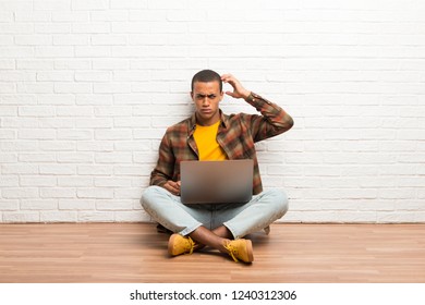 African american man sitting on the floor with his laptop having doubts while scratching head - Shutterstock ID 1240312306