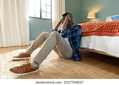 African american man sitting on bedroom floor, holding head in hands, feeling stressed, at home. mental health, anxiety, depression, solitude, contemplation, emotions - Powered by Shutterstock