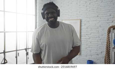 African american man smiling at the gym wearing headphones in a bright, modern gymnasium setting. - Powered by Shutterstock