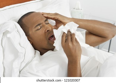 African American Man Sneezing Into Tissue Lying In Bed