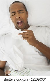 African American Man Sneezing Into Tissue Lying In Bed