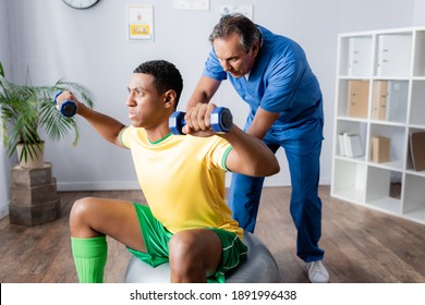 african american man in sportswear training with dumbbells on fitness ball near physiotherapist - Powered by Shutterstock