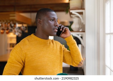 African American Man Standing In Kitchen At Home Talking On Smartphone And Looking Out Of Window. Inclusivity, Domestic Life, Spending Time Alone At Home.