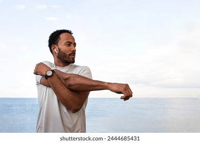 African American man stretching arm, warming up before workout and running session outdoors. Male exercising near the ocean. Health and fitness concept. - Powered by Shutterstock