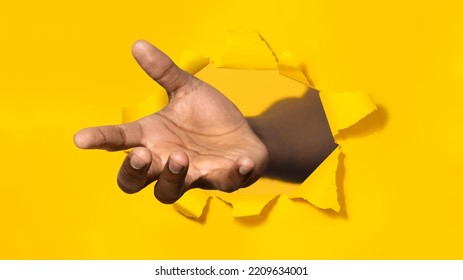 African american man stretching open palm through hole in torn yellow paper, offering helping hand, taking or giving something, asking for charity, reaching out for support - Shutterstock ID 2209634001