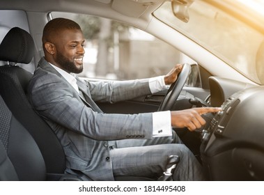 African American Man In Suit Driver Turning On Music In Car Before Moving. Cheerful Black Businessman Pushing Button On Functional Panel In His Car, Turning On Music Before Starting Business Trip