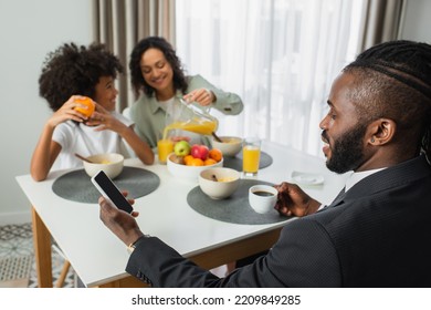 African American Man In Suit Using Smartphone With Blank Screen During Breakfast With Family On Blurred Background