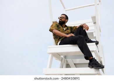 African american man in sunglasses relaxing on lifeguard tower on beach - Powered by Shutterstock