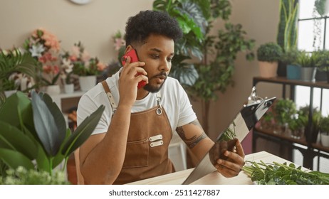 African american man talking on phone in flower shop while holding a clipboard, surrounded by green plants. - Powered by Shutterstock