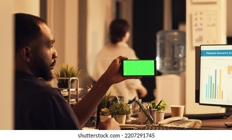 African American Man Using Smartphone With Greenscreen, Looking At Mobile Phone With Blank Copyspace Template At Sunset. Working With Isolated Mockup Screen And Chroma Key Display.