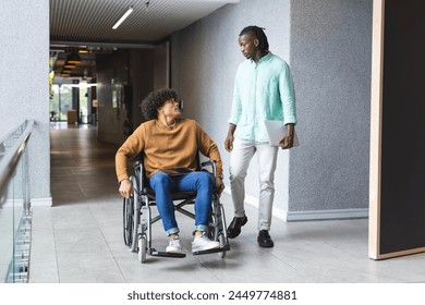 African American man walking beside biracial man in wheelchair in a modern business office. Both are young, first with dreadlocks and casual clothes, the second with curly hair, unaltered. - Powered by Shutterstock