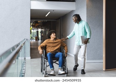 African American man walking beside biracial man in wheelchair, both smiling, in a modern business office. African American has dreadlocks, tablet in hand; biracial man has curly hair, unaltered. - Powered by Shutterstock
