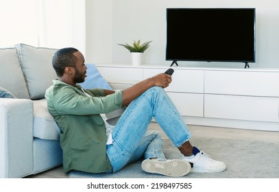 African American Man Watching Television, Turning On Plasma Flatscreen TV-set, Pointing Remote Control At Empty Screen, Mockup. Guy Switching Channels At Home