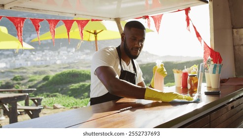 African american man wearing apron and gloves cleaning the food truck with disinfectant spray. hygiene and safety during coronavirus covid 19 pandemic concept - Powered by Shutterstock