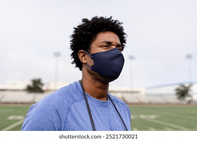 African American man wearing a mask on a sports field. The African American man in the mask is standing outdoors. The African American man is wearing a mask, looking into the distance in grass field. - Powered by Shutterstock