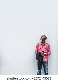 African American Man Wearing Red And White Shirt With Jeans Behind A White Wall Looking Up