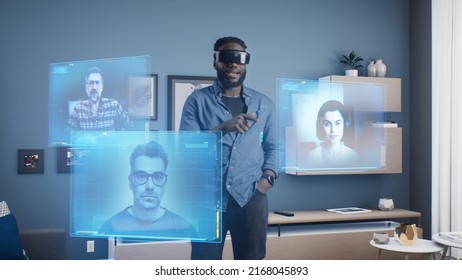 African American man wearing VR goggles at online business meeting in meta universe cyberspace talking with colleagues over video conference, holographic windows in front of him