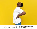african american man in white t-shirt holding on to his back and bending over yellow isolated background, the concept of back pain and problems with the spine
