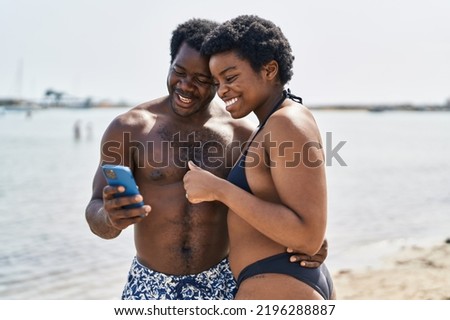 African american man and woman couple wearing swimsuit using smartphone at seaside
