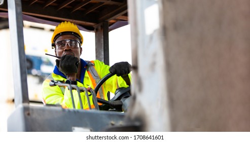 African American Man at work. Professional operation engineering. Young worker forklift driver wearing safety goggles and hard hat sitting in vehicle in warehouse. Walkie talkie communication - Powered by Shutterstock
