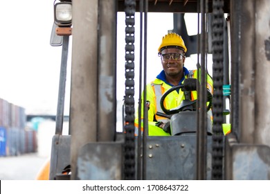 African American Man At Work. Professional Operation Engineering. Young Worker Forklift Driver Wearing Safety Goggles And Hard Hat Sitting In Vehicle In Warehouse