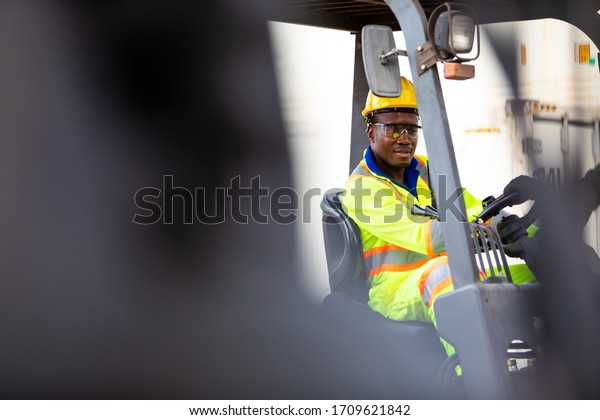 African American Man at work.\
Professional operation engineering. Young worker forklift driver\
wearing safety goggles and hard hat sitting in vehicle in\
warehouse