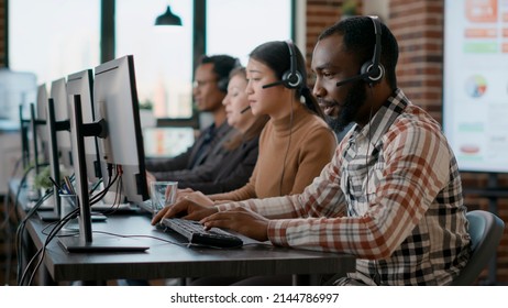 African American Man Working At Call Center Office To Help People With Telemarketing Assistance. Male Employee Using Headphones And Microphone At Customer Care Service. Tripod Shot.