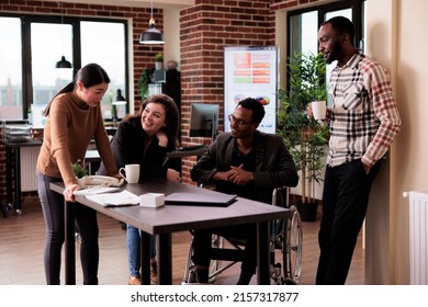 African American Manager With Physical Disability Laughing With Coworkers, Working In Disability Friendly Office. Businesspeople And Wheelchair User Chatting On Break In Startup Workplace.