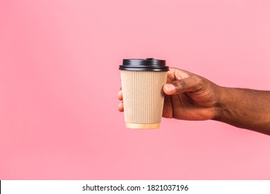 African American Man's Hand Holding Paper Coffee Cup Isolated Over Pink Background. 