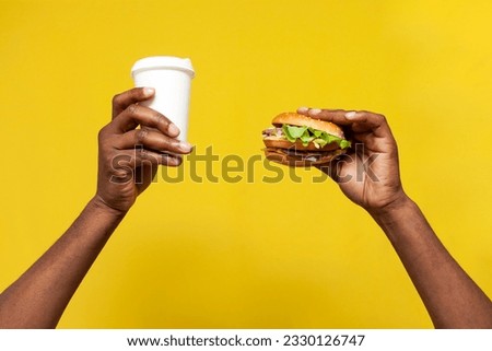 african american man's hands hold delicious fresh burger and paper cup coffee on yellow isolated background, hand offers and advertises fast food and drink, close-up