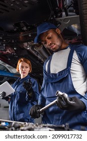 African american mechanic holding wrench near blurred colleague with digital tablet and car in garage