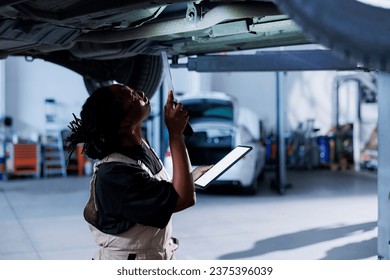 African american mechanic uses mockup tablet while changing old car brake fluid with new one in repair shop. BIPOC woman holding Isolated screen device in garage while doing vehicle checkup - Powered by Shutterstock