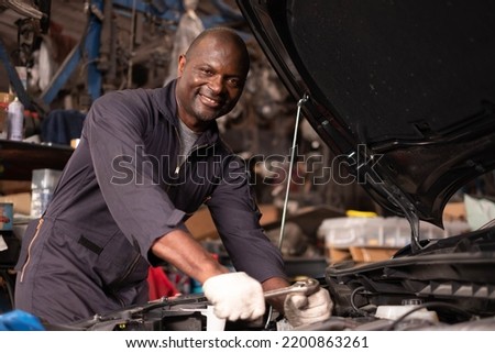 African american  mechanics - man examining car engine. Auto mechanic working in garage.Car Mechanic Detailed Vehicle Inspection. Auto Service Center Theme.