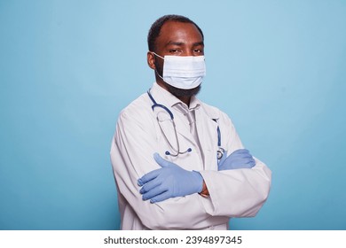 African american medic in hospital uniform wearing protective face mask and posing with his arms crossed. Portrait of black male doctor with stethoscope and medical protective gear. - Shutterstock ID 2394897345