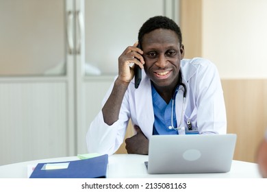 African American medical male doctor talking mobile phone and working with laptop at table office in hospital. - Powered by Shutterstock