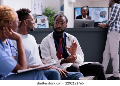 African american medical team consulting man sitting in waiting room at facility reception lobby. Doctor and assistant talking to patient about disease diagnosis and treatment, healthcare support.
