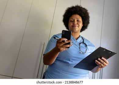 African american mid adult female nurse using smart phone while holding clipboard in hospital. unaltered, healthcare worker, wireless technology, expertise and occupation concept. - Powered by Shutterstock